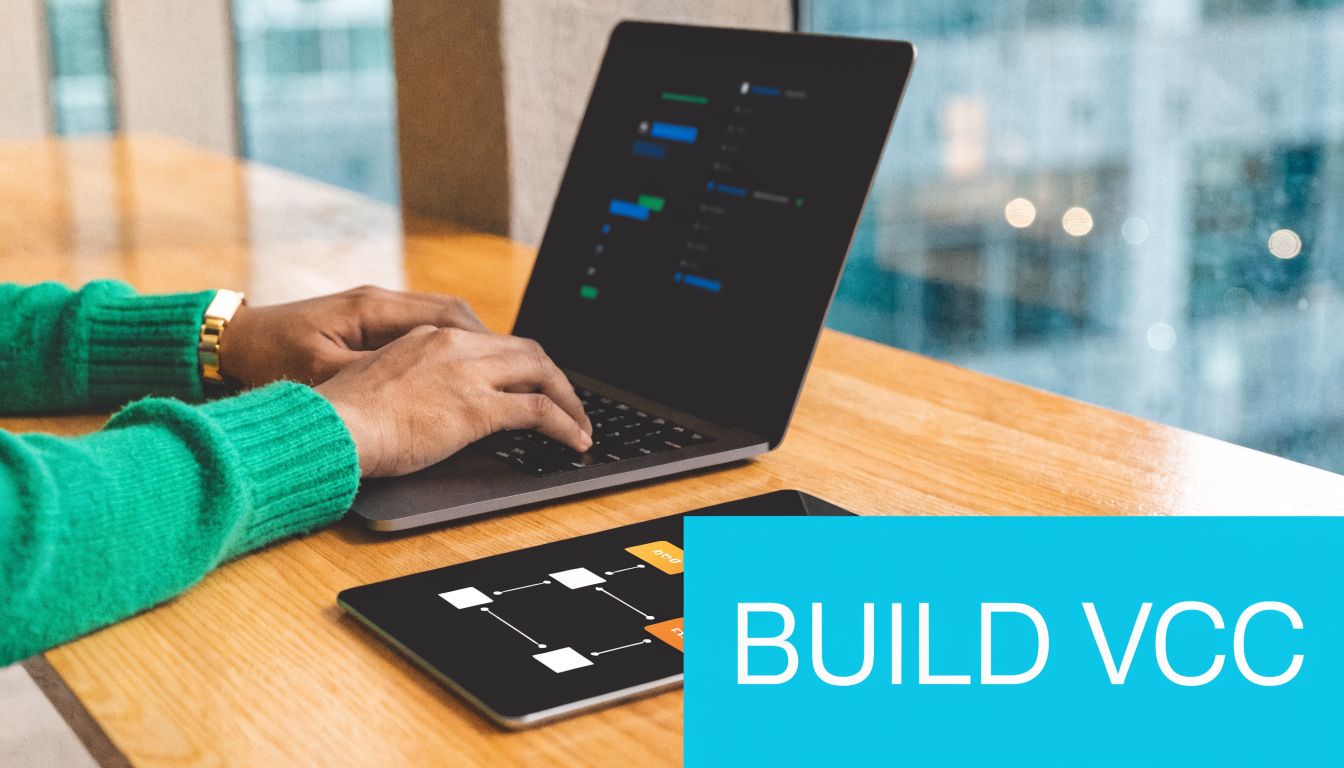 A person wearing a green sweater working on a laptop with a digital flowchart on a tablet