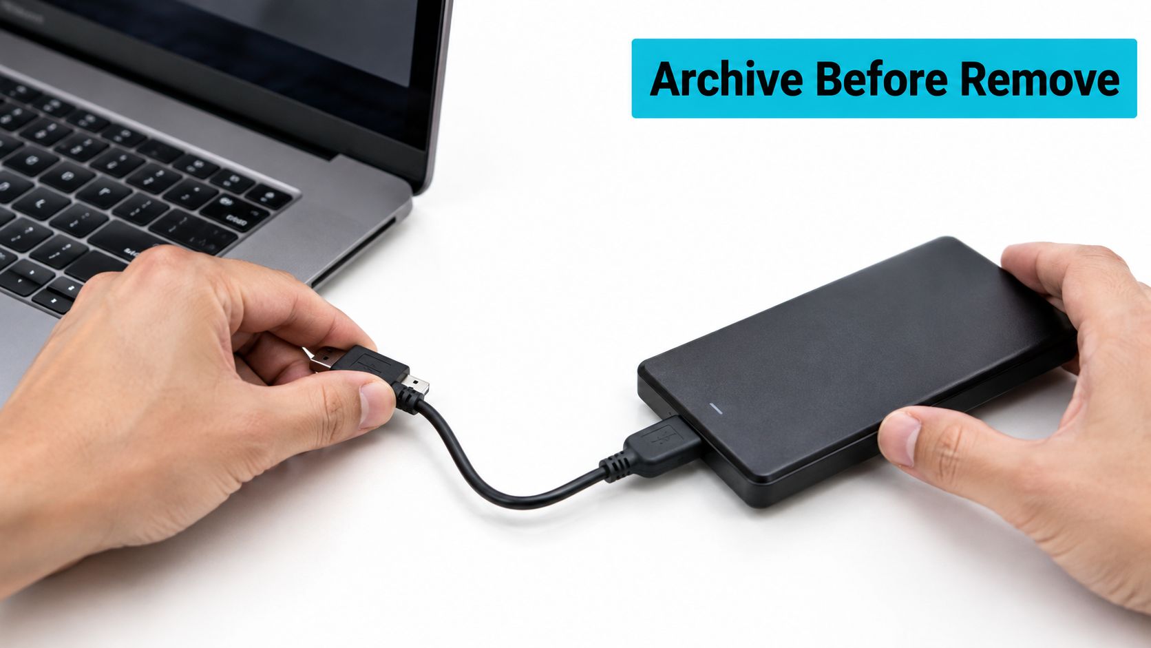 A person disconnecting a portable hard drive from a silver laptop on a white desk surface.